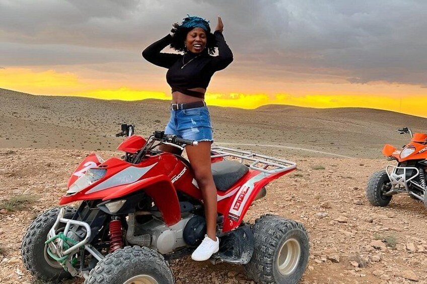 A person on a red ATV in a desert landscape with a sunset in the background. 5