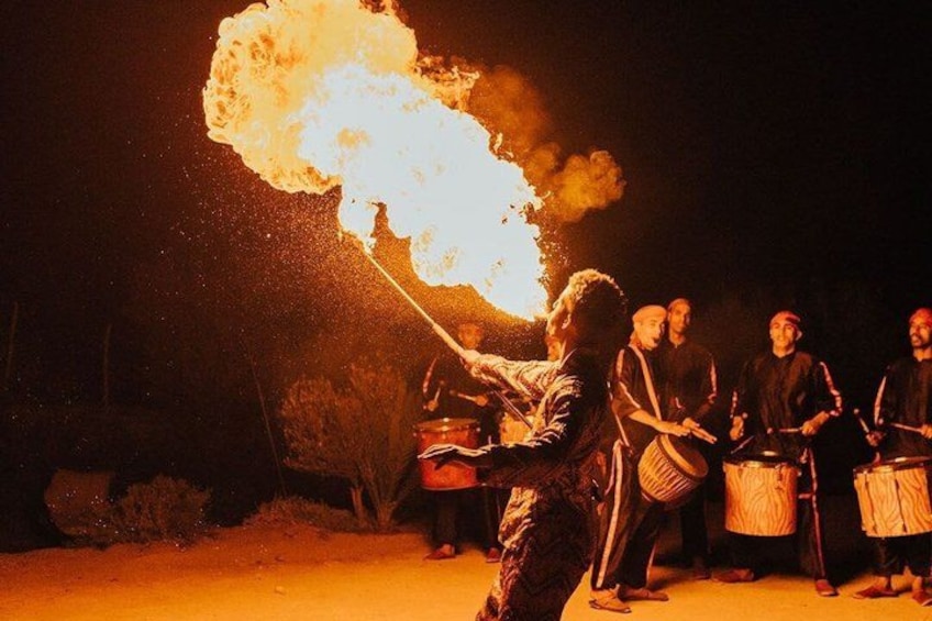 A person with a flaming torch, a group of people in traditional attire, and a desert landscape at night. 1