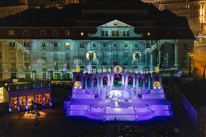 A grand building with a stage and statues, illuminated at night. 4