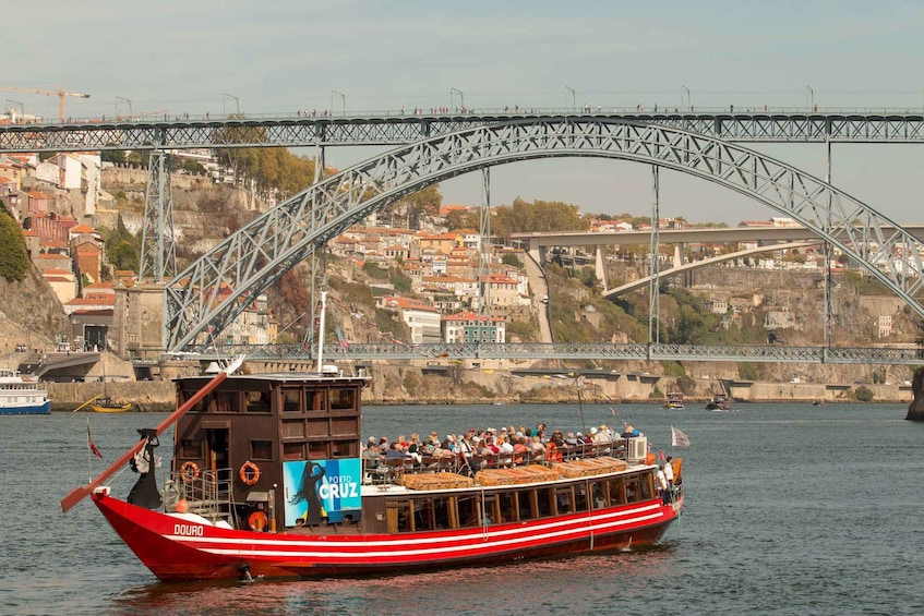 A red boat with passengers, a bridge, and a hillside town in the background. 2