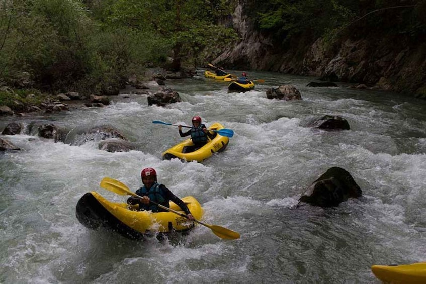 Three people kayaking on a river with rapids, surrounded by rocky terrain and greenery. 3