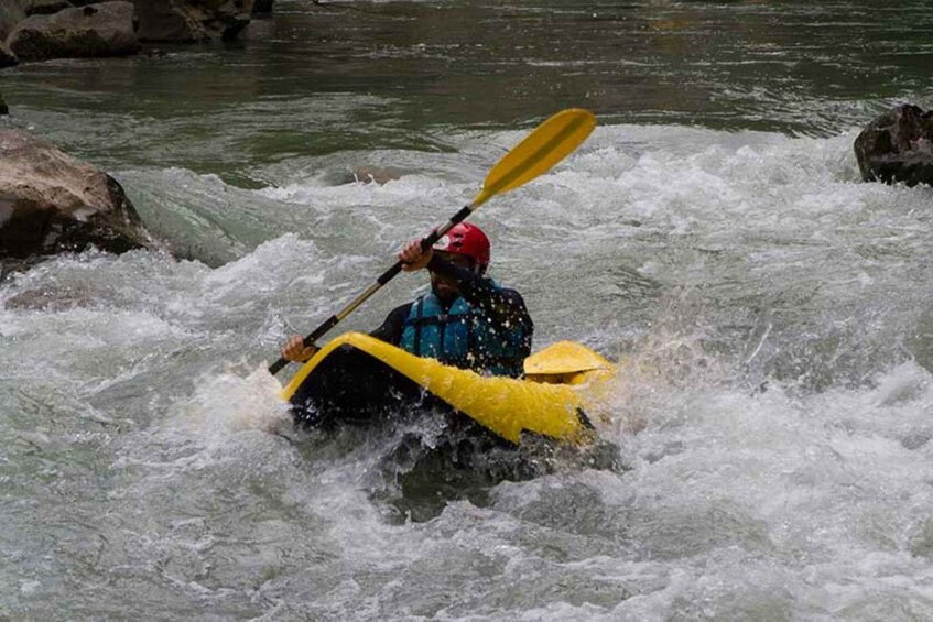 A person kayaking through a river with rapids, wearing a life jacket and a helmet. 4