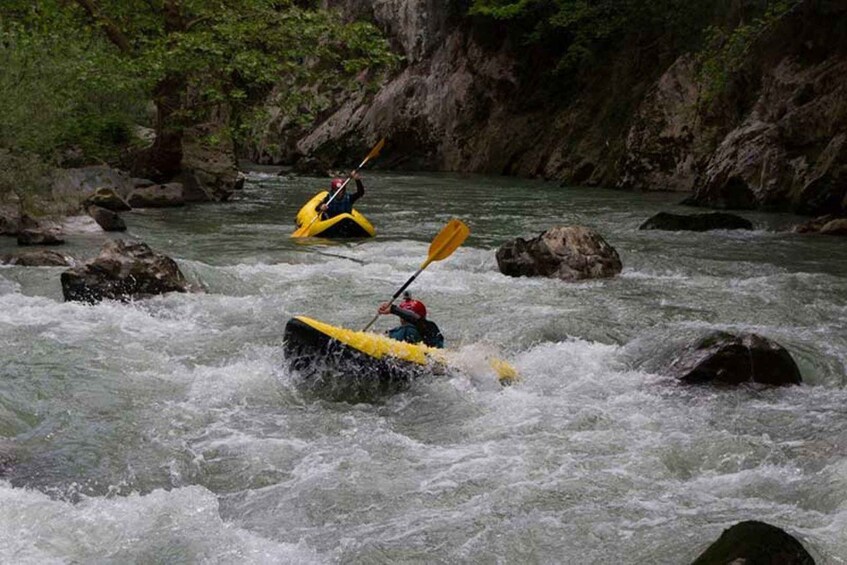 Two kayakers navigating a river with rapids, surrounded by rocky terrain and greenery. 2