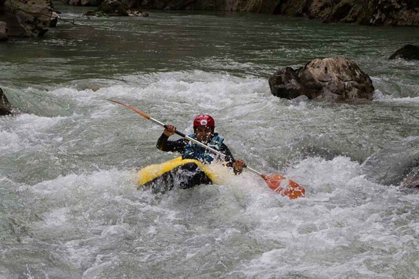 A kayaker navigating through a river with rapids, wearing a helmet and using a paddle. 5