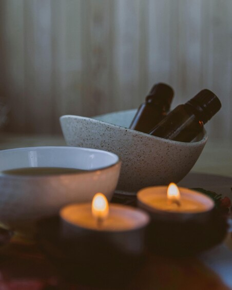 A bowl with bottles, a lit candle, and a cup on a table. 3