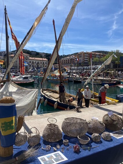 A harbor with boats, a market stall with woven baskets and jewelry, and buildings in the background. 1
