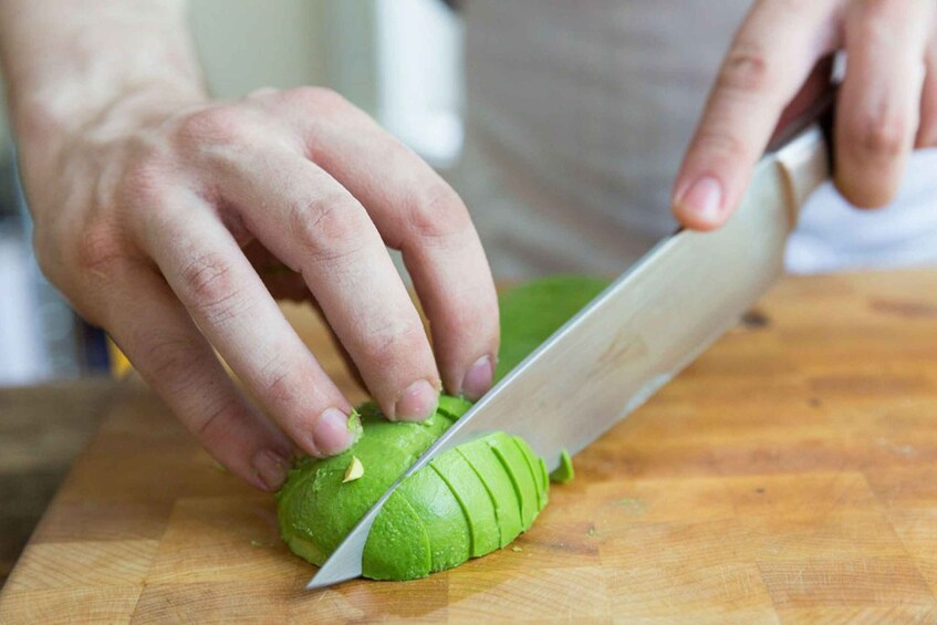 A person slicing a green vegetable on a wooden cutting board. 4