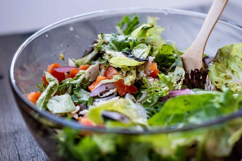 A salad bowl with mixed greens, tomatoes, and a wooden spoon. 1