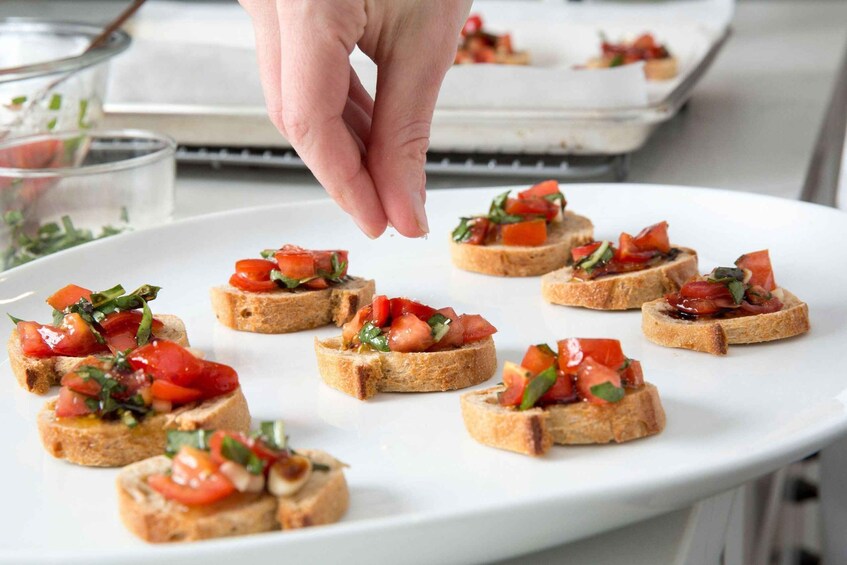 A hand placing a piece of toast with tomato and basil on a plate. 5