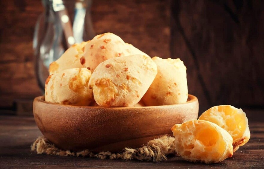 A wooden bowl filled with cheese bread, with a rustic background. 3