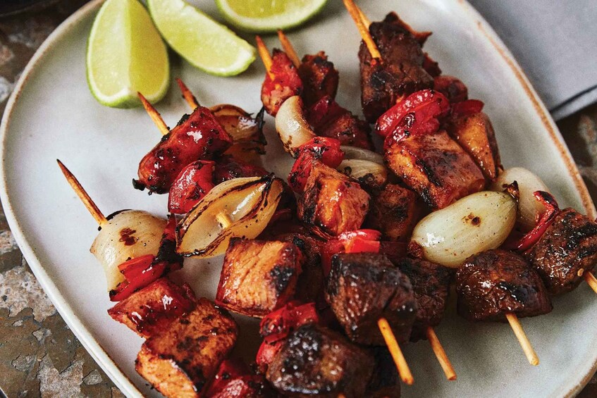 Skewers of grilled meat and vegetables on a plate with lime wedges. 1