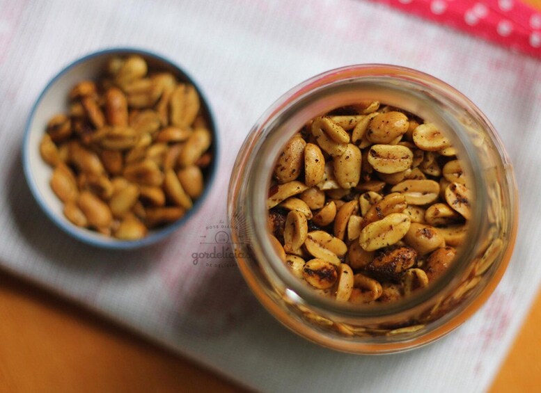A glass jar and a bowl of roasted peanuts on a cloth. 2