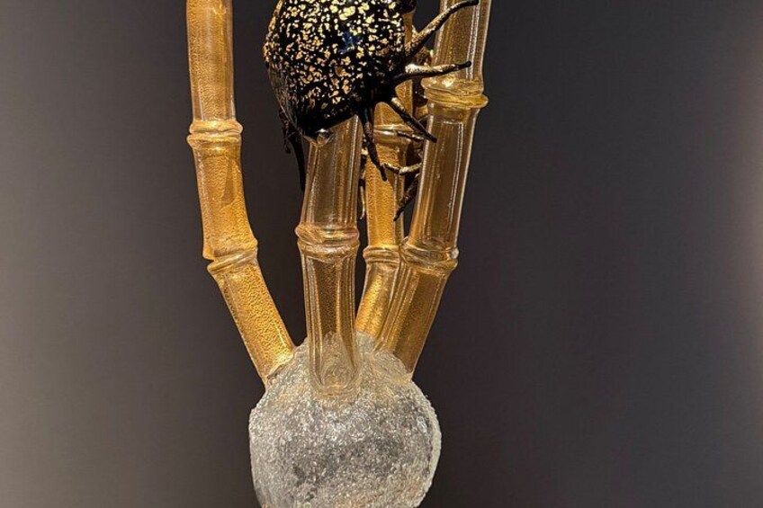A sculpture of a black insect on a golden structure with a textured base. 3