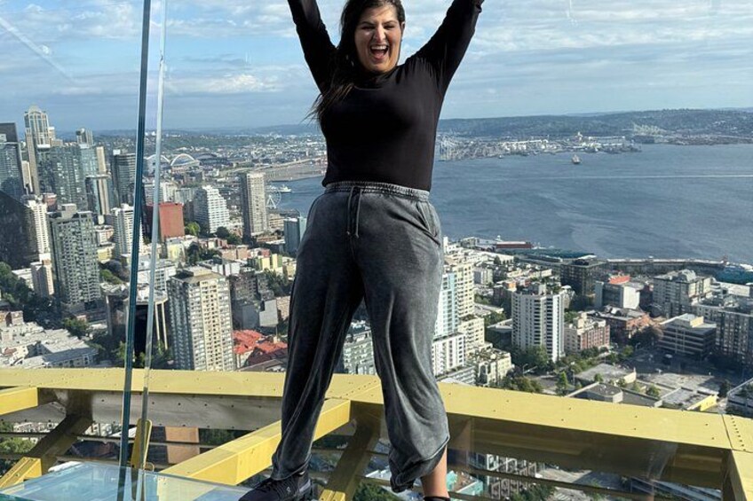 A person standing on a glass floor with a cityscape in the background. 5