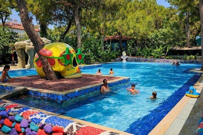 A swimming pool with colorful mosaic tiles, a large decorative shell, and trees in the background. 3