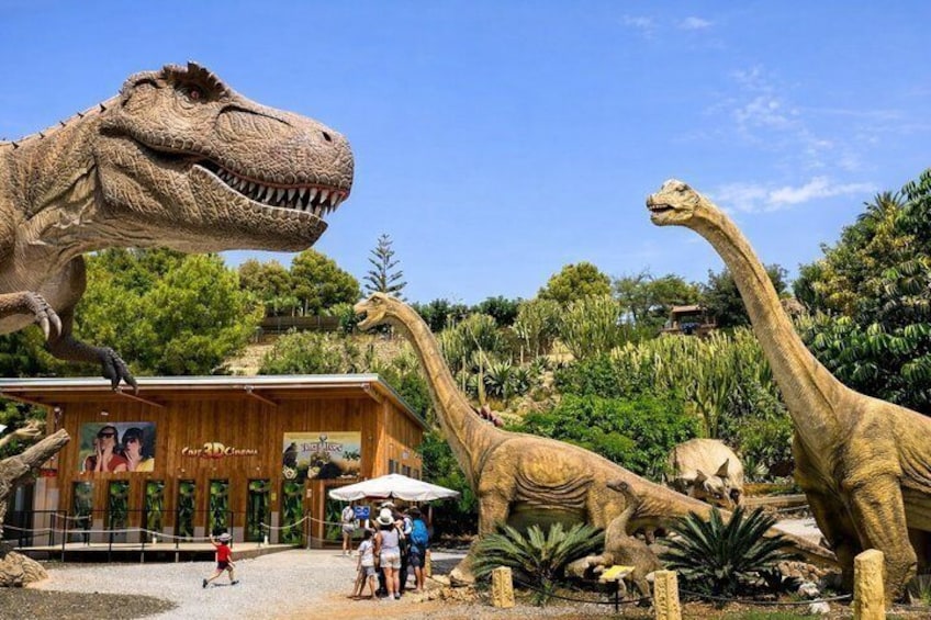 A dinosaur exhibit with a large T-Rex and a long-necked dinosaur in front of a wooden building. 4