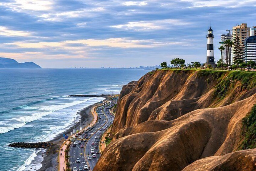 A coastal road with a lighthouse, cliffs, and a city skyline in the distance. 1