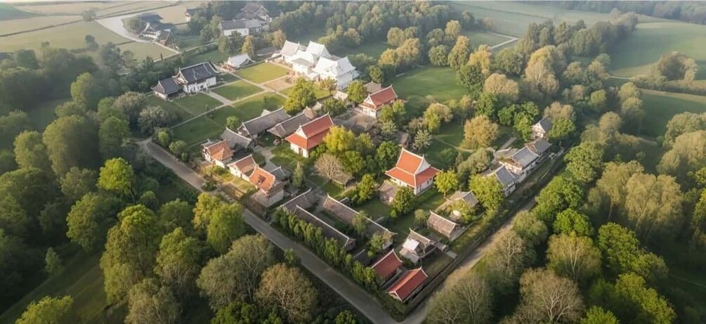 An aerial view of a traditional village with red-roofed houses, a large white building, and surrounding greenery. 3