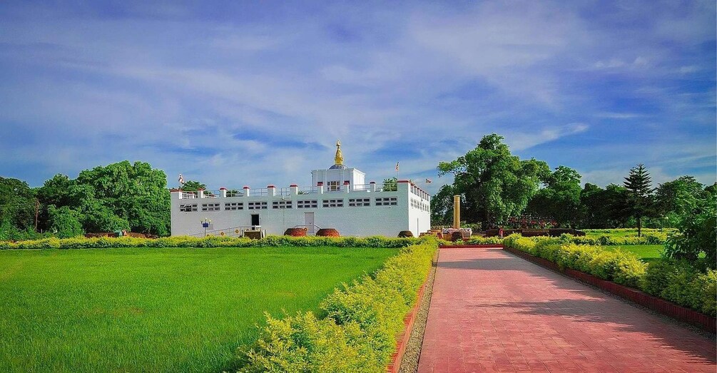 A white building with a golden dome, surrounded by a well-maintained garden and a red pathway. 1