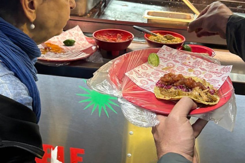 A person holding a wrapped taco with a lime wedge on a red plate. 3