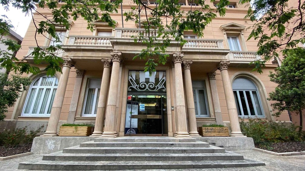 A building with classical architecture, featuring columns, a balcony, and a large entrance. 5