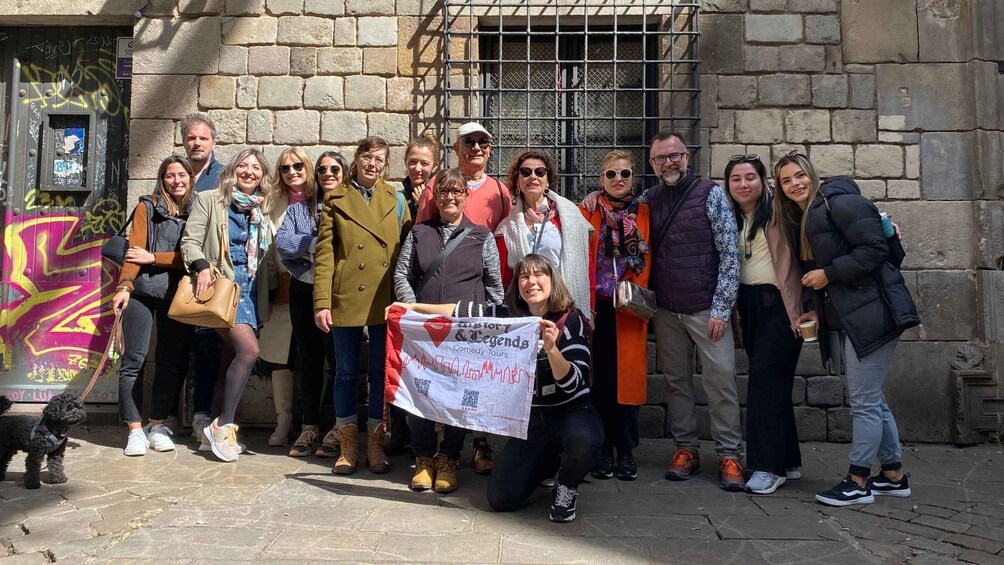 A group of people standing in front of a stone building with graffiti, holding a banner that reads 'History & Legends Comedy Tours.' 3