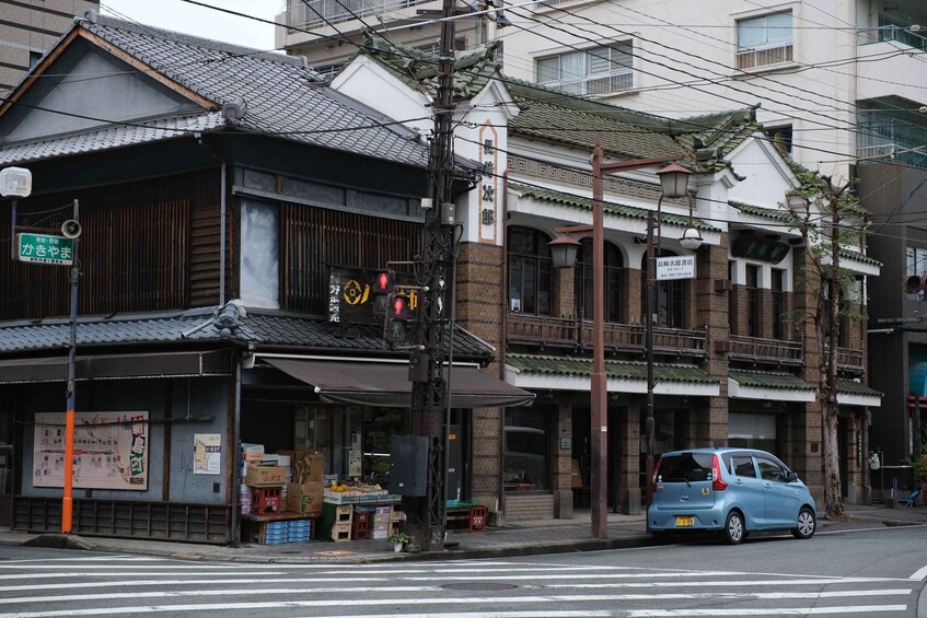 A street scene with traditional Japanese architecture, a blue car parked on the side, and a pedestrian crossing. 3