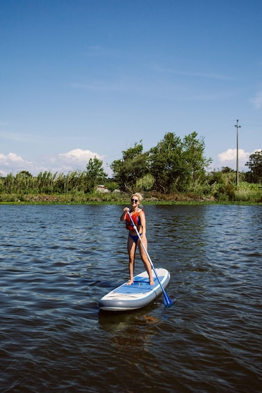 A person paddleboarding on a calm river with trees and a clear sky in the background. 1
