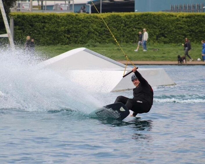 A person wakeboarding on a body of water with a white structure in the background. 3