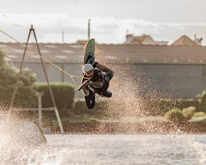 A person windsurfing, airborne above water, with a clear sky and distant buildings in the background. 5
