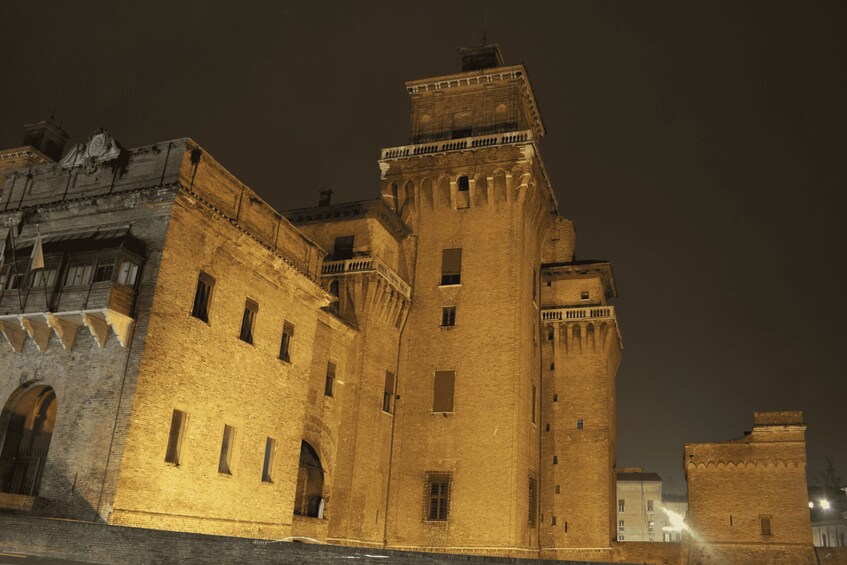 A historic brick building with arched windows and a prominent tower at night. 1