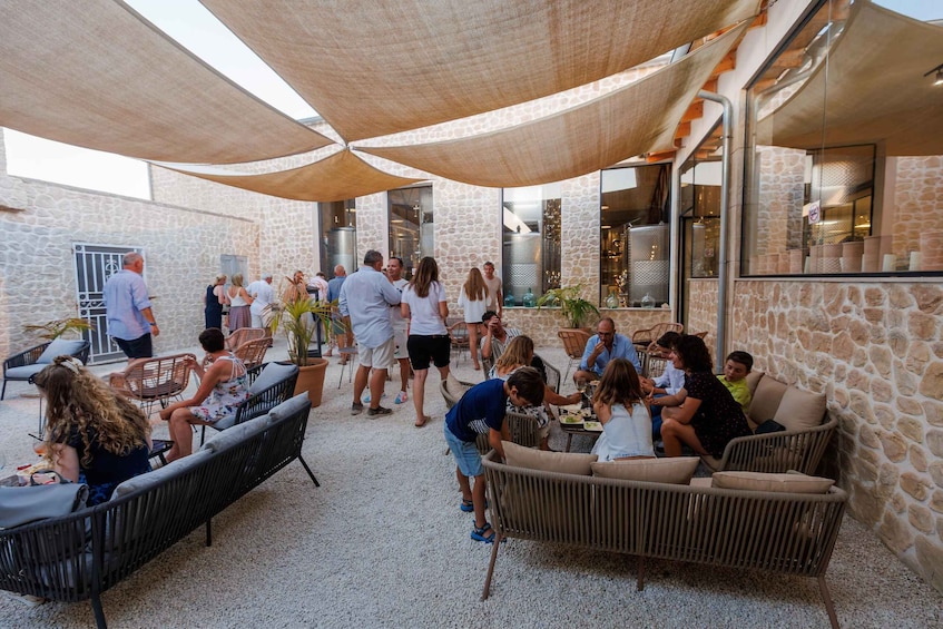 A group of people dining outdoors under shaded canopies, with stone walls and wicker furniture. 4