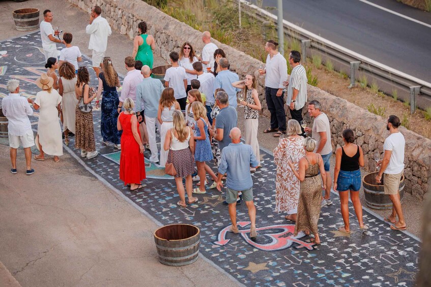 A group of people standing on a patterned pavement near a stone wall and a road. 3