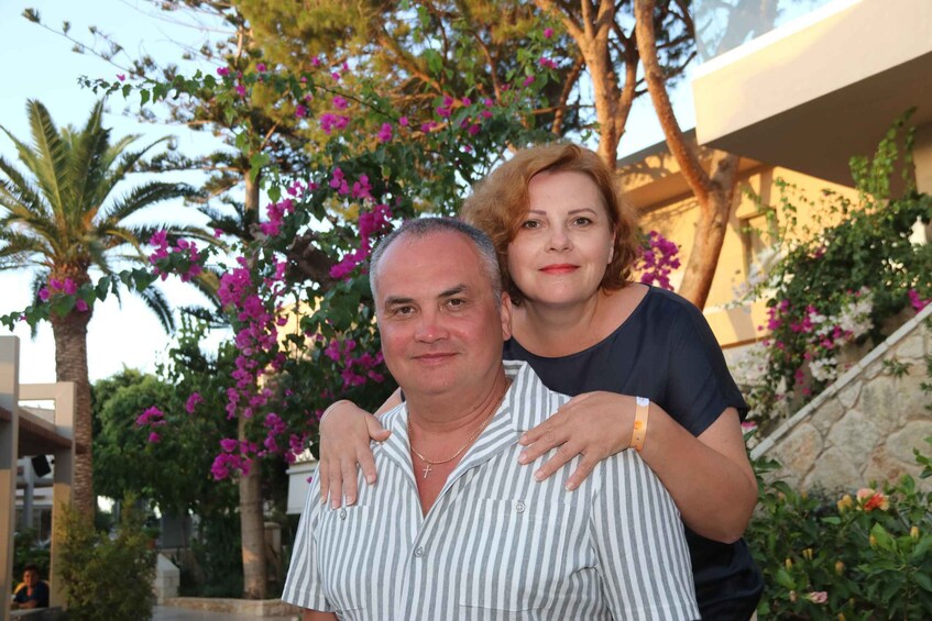 A man and a woman standing in front of a building with pink flowers and palm trees. 4