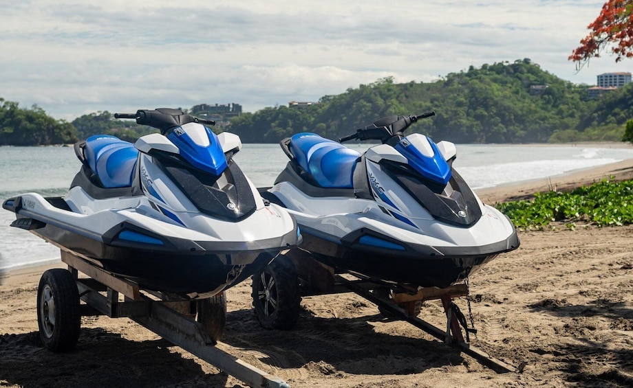 Two jet skis on a beach with a forested hill in the background. 4