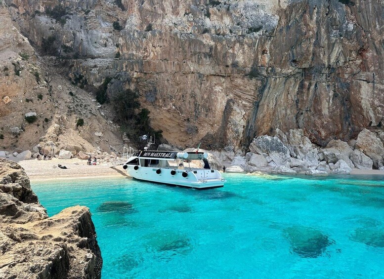 A boat named 'Mon Maestrale' anchored near a rocky coastline with clear turquoise waters. 2