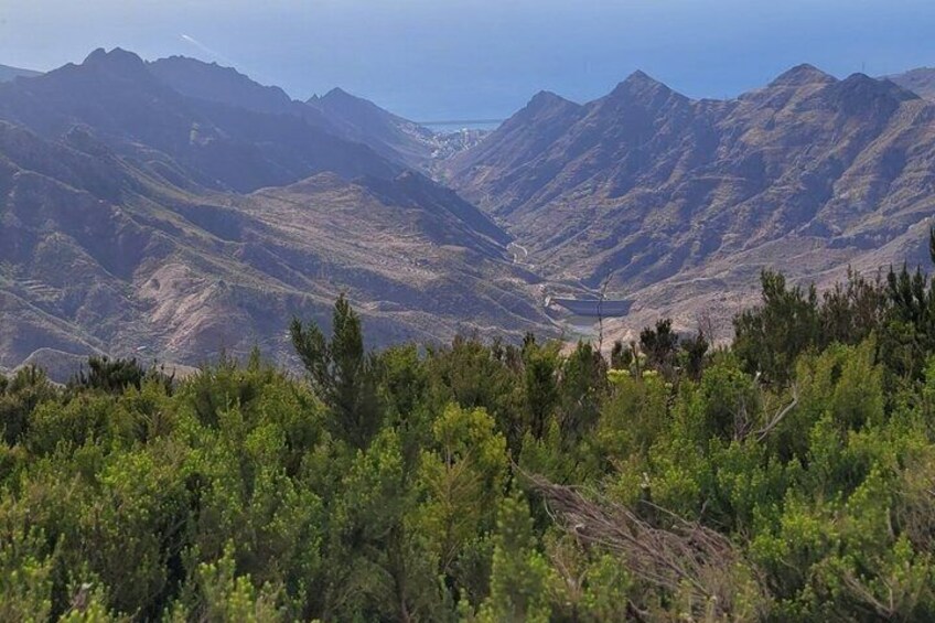 A mountainous landscape with dense green vegetation in the foreground and a valley with a small body of water in the distance. 5