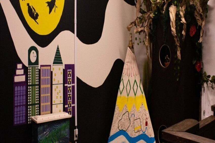 A cityscape mural with buildings and a clock tower, a colorful hat with a bird design, and a wall with greenery and flowers. 2