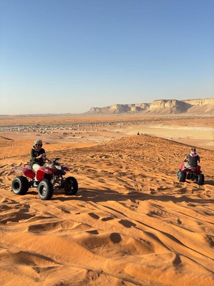 Two people riding quad bikes in a desert with sand dunes and distant mountains. 4