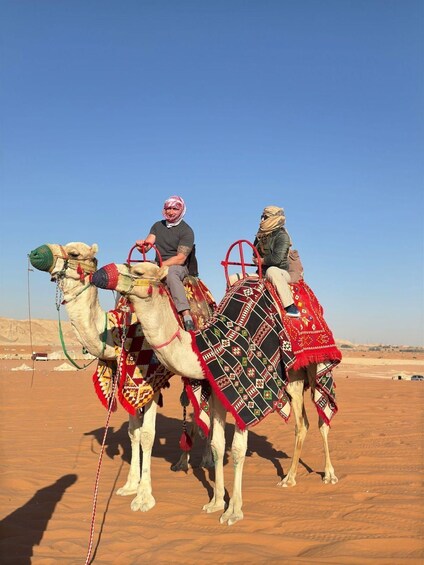 Two camels with riders in a desert landscape. 1