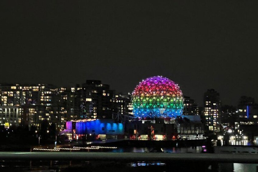 A cityscape at night with a prominent spherical building illuminated with multicolored lights. 4