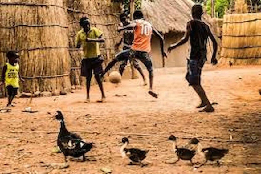 Children playing soccer in a rural setting with a thatched-roof structure in the background. 3