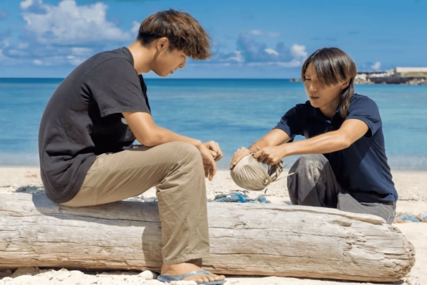 Two people sitting on a log by the beach, with the ocean in the background. 1
