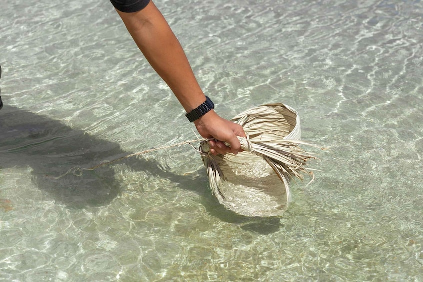 A person holding a woven basket over clear shallow water. 3