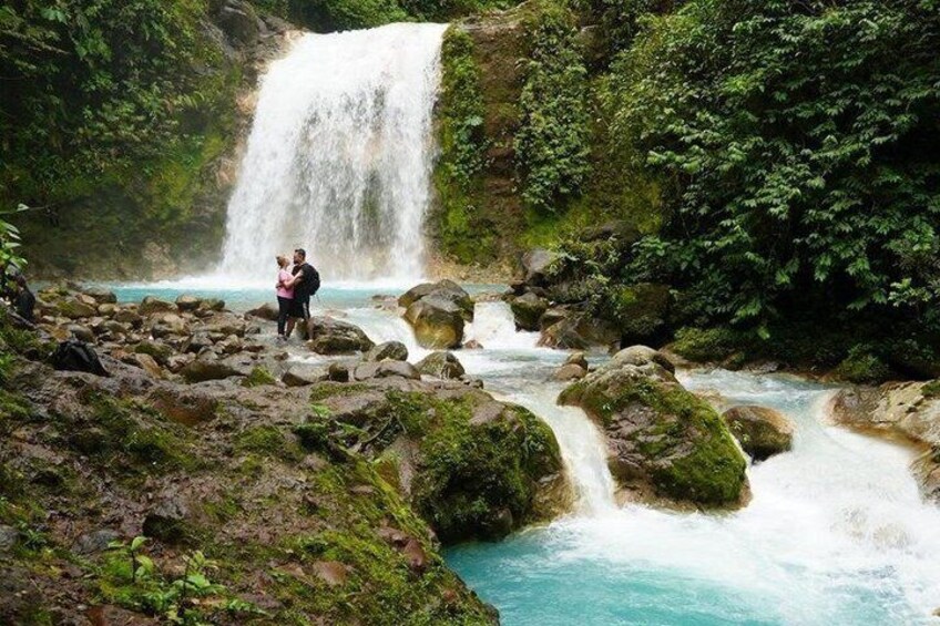 A waterfall, a river, and a couple standing on rocks. 4