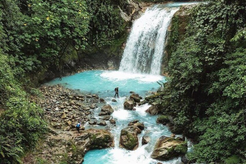 A waterfall, clear blue pool, and rocky terrain surrounded by greenery. 1