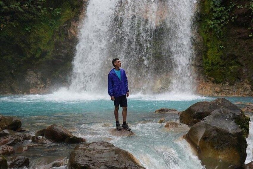 A person standing on rocks by a waterfall. 5