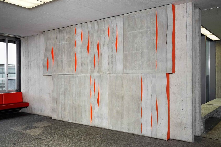 A modern interior with a concrete wall featuring orange streaks, a red bench, and a glass door. 4