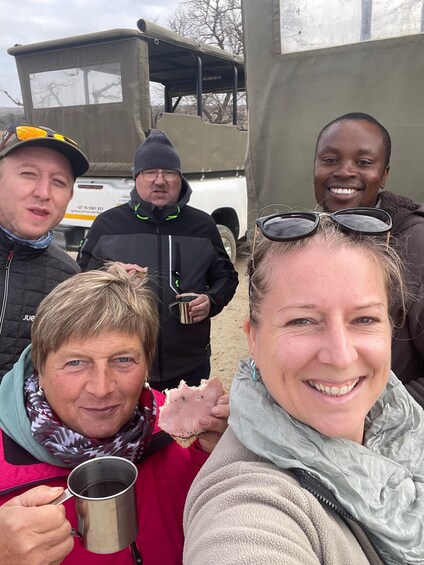 A group of people outdoors, some holding mugs, with a vehicle and a tent in the background. 3