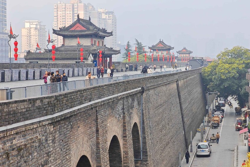 A traditional Chinese architectural complex with a stone bridge, red lanterns, and a cityscape in the background. 1